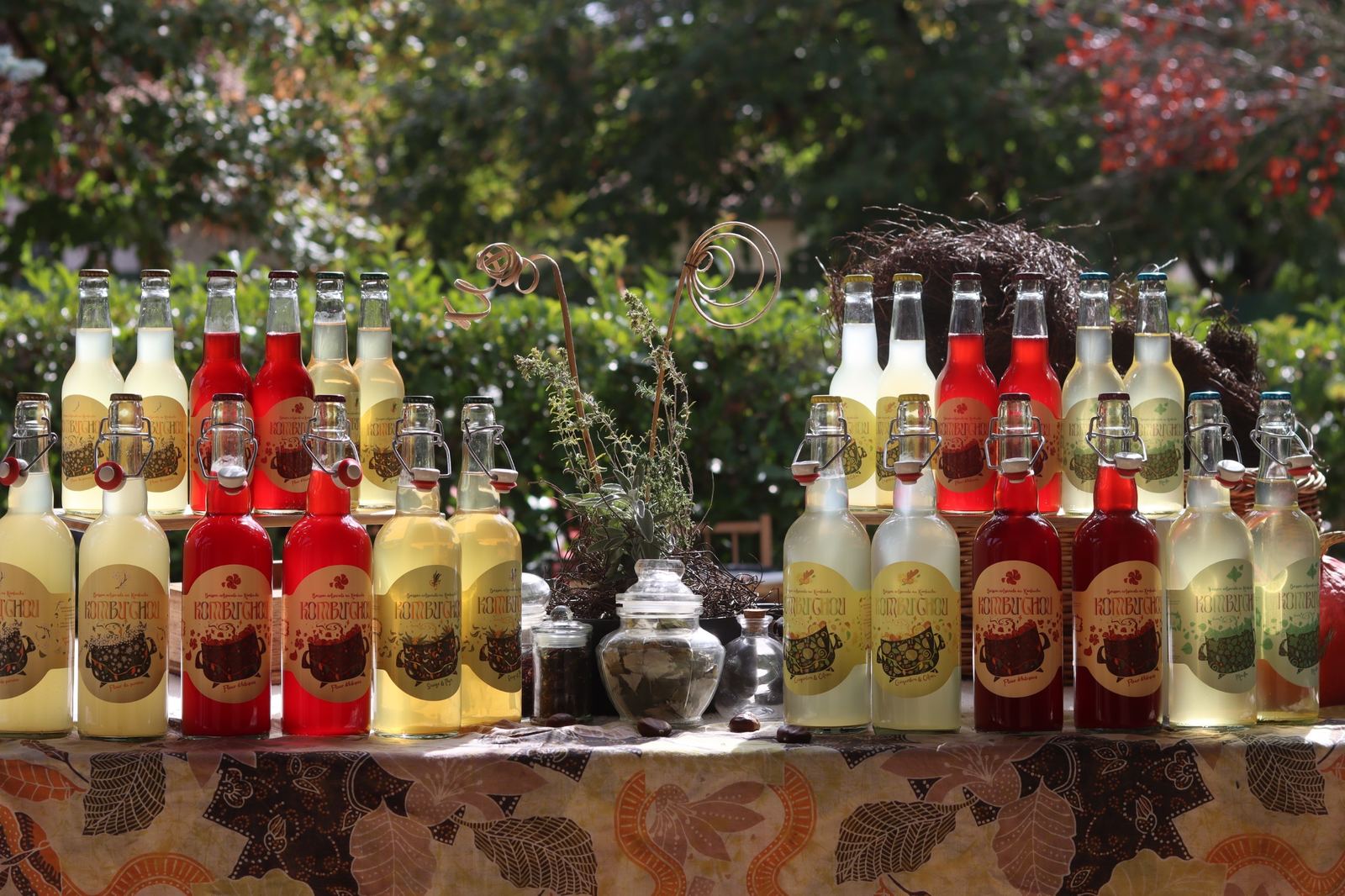 Le stand Kombuchou au marché : bouteilles de kombucha rouges et dorées alignées sur une nappe